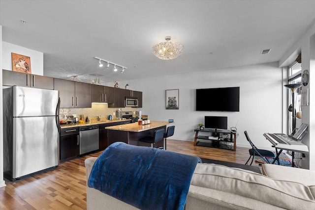 kitchen featuring dark brown cabinetry, appliances with stainless steel finishes, backsplash, light hardwood / wood-style flooring, and a kitchen island