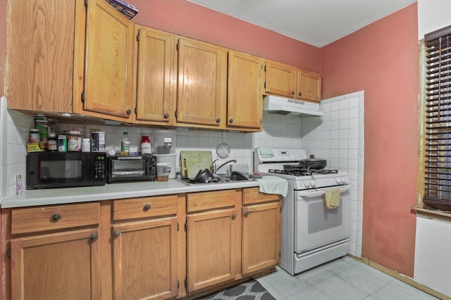 kitchen with white range with gas stovetop, light tile patterned floors, sink, and backsplash