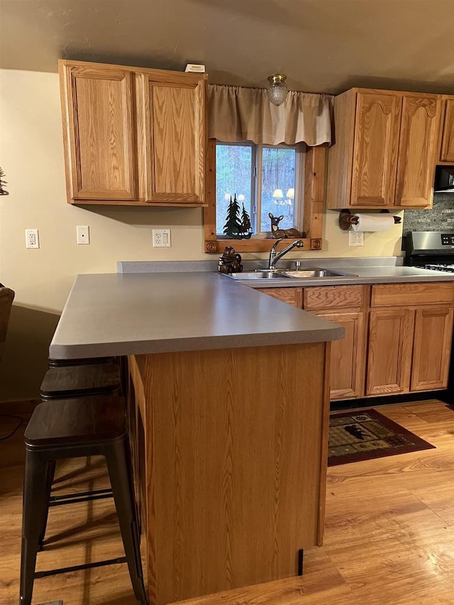 kitchen with ventilation hood, range, sink, light hardwood / wood-style floors, and a breakfast bar area