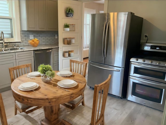 kitchen with stainless steel appliances, light stone counters, sink, gray cabinets, and light wood-type flooring