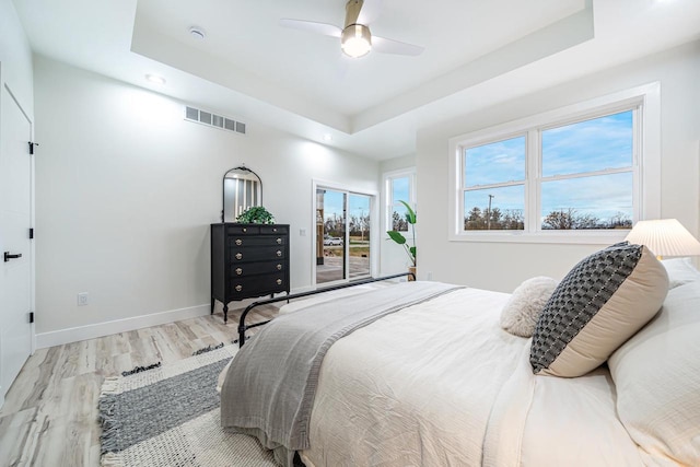 bedroom with light wood-type flooring, ceiling fan, and a tray ceiling