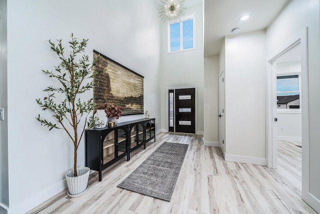 entryway with light wood-type flooring, a high ceiling, and an inviting chandelier