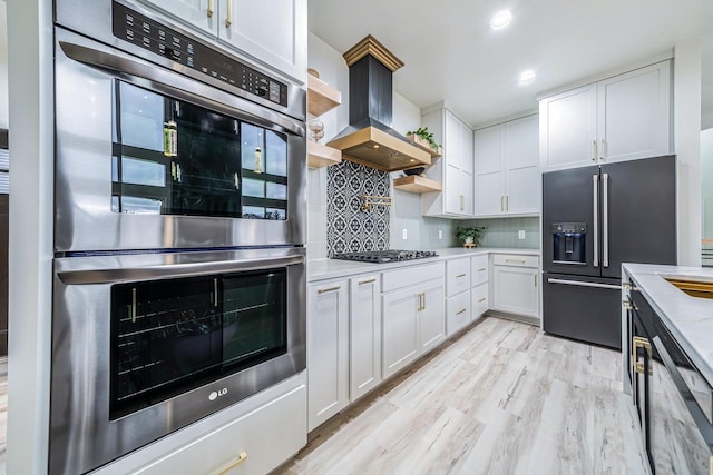 kitchen with tasteful backsplash, appliances with stainless steel finishes, light hardwood / wood-style floors, white cabinets, and custom exhaust hood