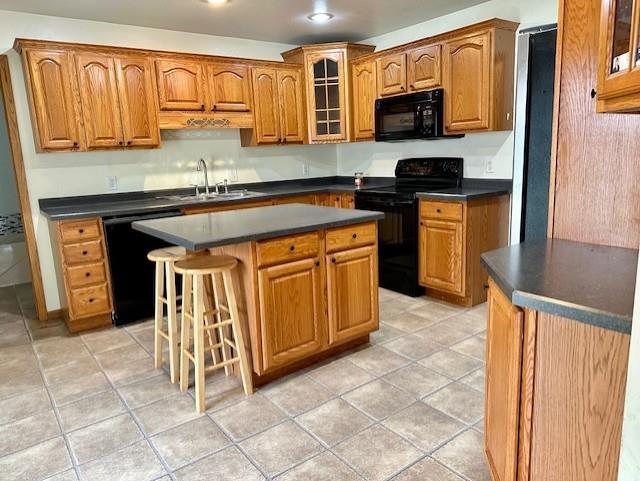 kitchen with black appliances, light tile patterned floors, sink, a breakfast bar area, and a center island