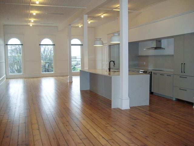 kitchen featuring white cabinetry, sink, wall chimney exhaust hood, light hardwood / wood-style floors, and a kitchen island with sink