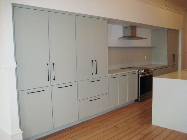 kitchen featuring wall chimney exhaust hood, stainless steel range with electric stovetop, light wood-style floors, light countertops, and modern cabinets