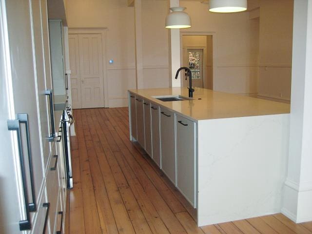 kitchen with light wood-type flooring, gray cabinetry, sink, decorative light fixtures, and an island with sink