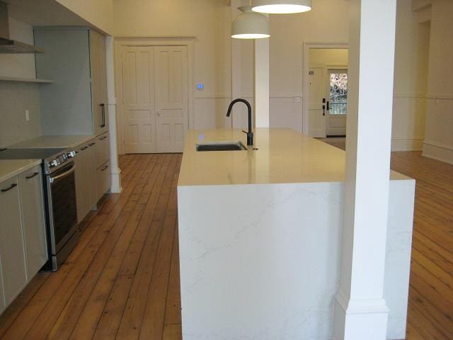 kitchen featuring stainless steel range with electric cooktop, sink, hardwood / wood-style flooring, pendant lighting, and an island with sink