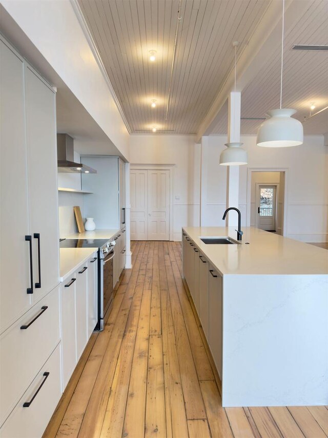 kitchen with stainless steel electric range, a sink, modern cabinets, wall chimney range hood, and light countertops