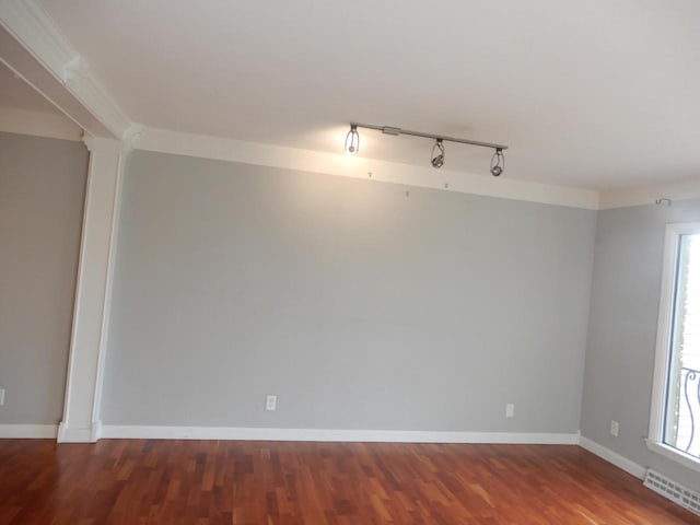 spare room featuring dark wood-type flooring, ornate columns, track lighting, and ornamental molding