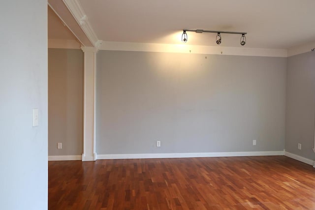 spare room featuring ornate columns, rail lighting, dark hardwood / wood-style floors, and crown molding