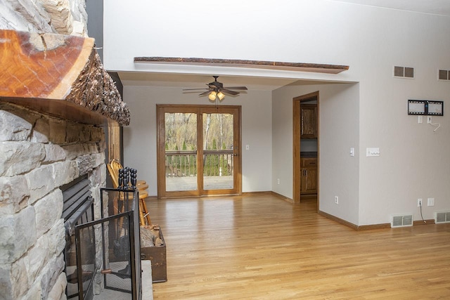 living room with light hardwood / wood-style flooring, ceiling fan, and a stone fireplace