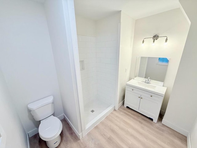 bathroom featuring hardwood / wood-style flooring, vanity, toilet, and a tile shower