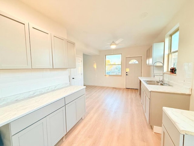 kitchen with sink, gray cabinets, ceiling fan, backsplash, and light hardwood / wood-style flooring