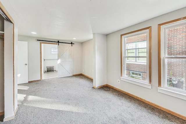 carpeted empty room featuring radiator and a barn door