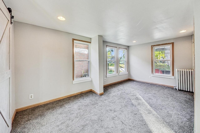 spare room with a barn door, radiator, and carpet