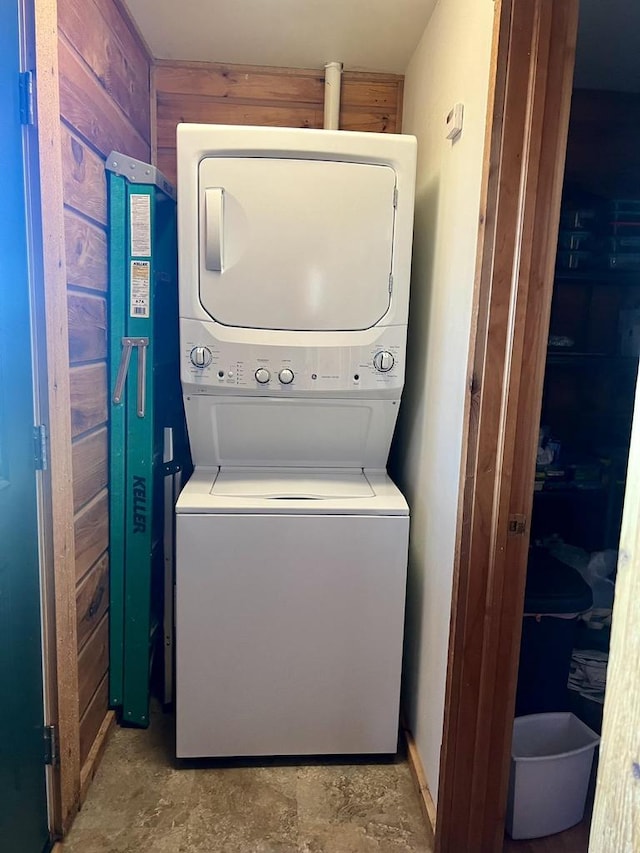 clothes washing area featuring stacked washer / dryer and wooden walls