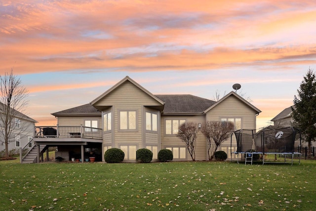 back house at dusk with a wooden deck, a yard, and a trampoline