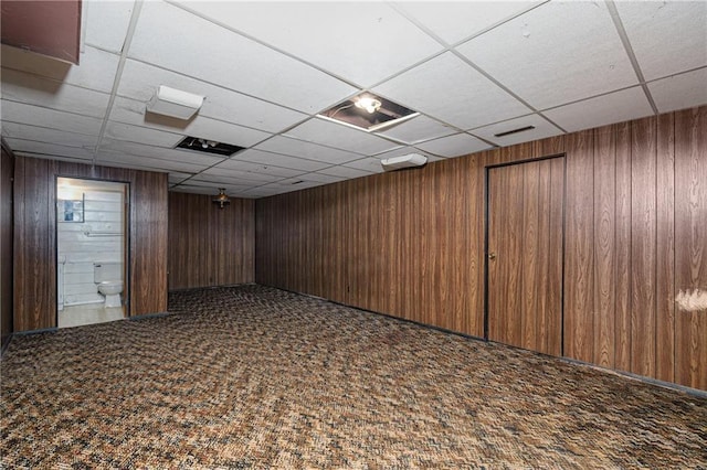 basement with wooden walls, a drop ceiling, and carpet