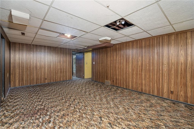 basement featuring wood walls, a paneled ceiling, and carpet flooring