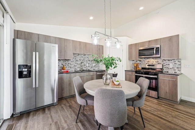 kitchen with dark wood-type flooring, pendant lighting, appliances with stainless steel finishes, and decorative backsplash