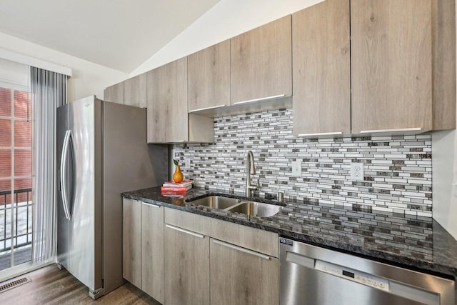 kitchen featuring sink, appliances with stainless steel finishes, dark stone countertops, lofted ceiling, and dark hardwood / wood-style flooring