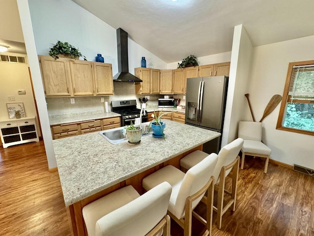 kitchen featuring a kitchen bar, dark hardwood / wood-style flooring, lofted ceiling, wall chimney exhaust hood, and appliances with stainless steel finishes