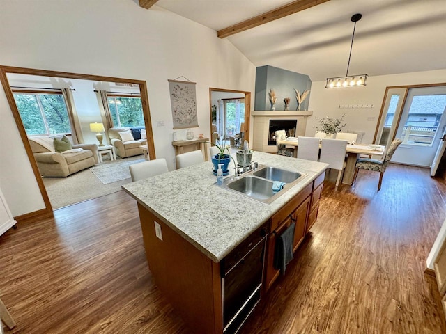 kitchen with vaulted ceiling with beams, a center island with sink, pendant lighting, sink, and dark wood-type flooring