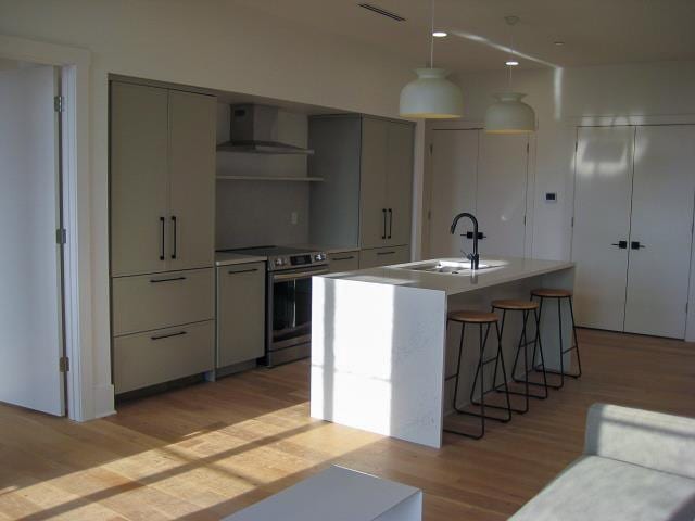 kitchen with a center island with sink, wall chimney range hood, sink, electric range, and light hardwood / wood-style flooring