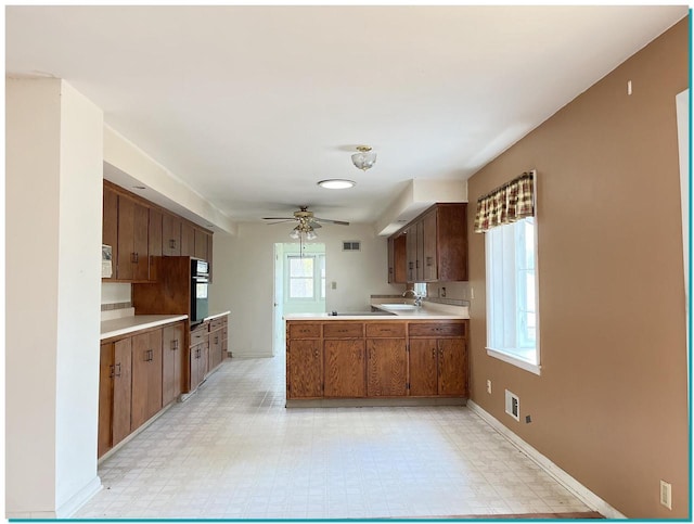 kitchen with sink, kitchen peninsula, stovetop, ceiling fan, and oven