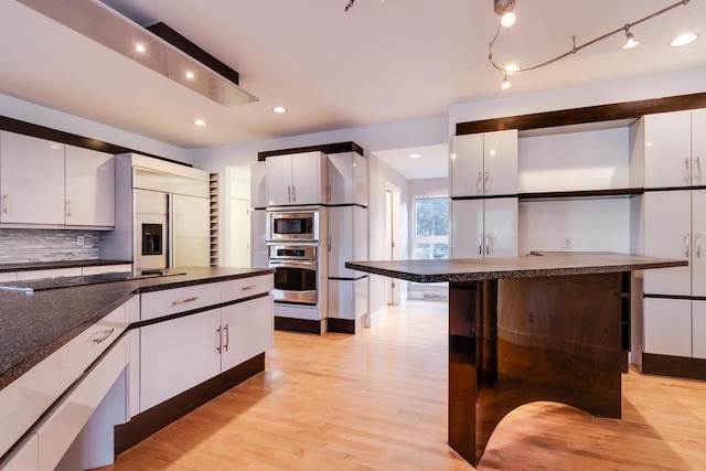 kitchen with backsplash, built in appliances, light hardwood / wood-style flooring, white cabinets, and a kitchen island