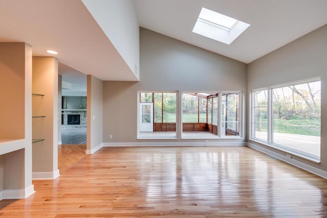 unfurnished living room with light wood-type flooring, a skylight, and high vaulted ceiling