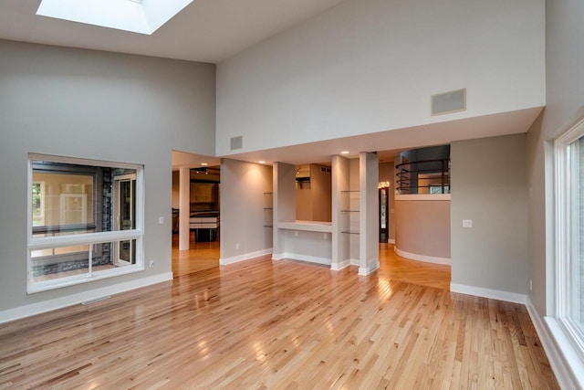 unfurnished living room with light hardwood / wood-style floors, high vaulted ceiling, and a skylight