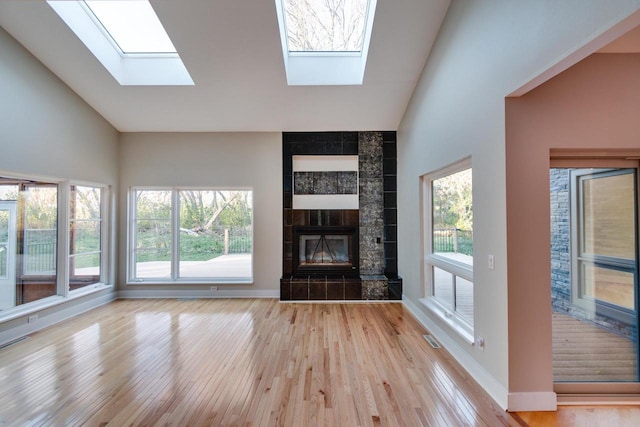 unfurnished living room featuring light hardwood / wood-style floors, high vaulted ceiling, and a tiled fireplace