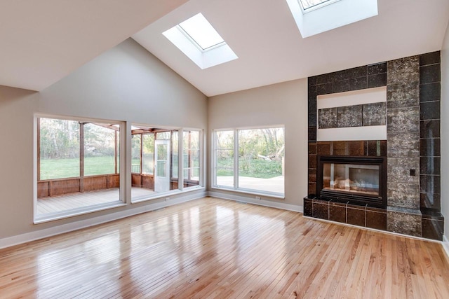 unfurnished living room with a tile fireplace, light wood-type flooring, and high vaulted ceiling