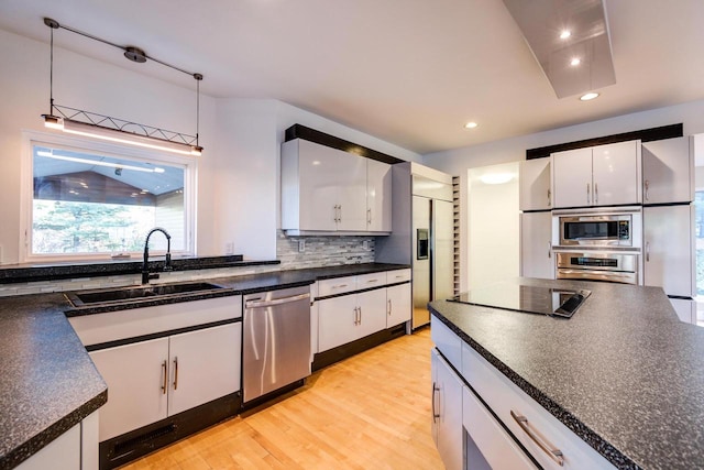 kitchen with white cabinets, built in appliances, decorative light fixtures, and light hardwood / wood-style flooring