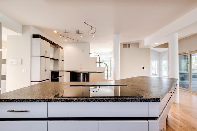 kitchen with white cabinetry, black electric stovetop, a spacious island, and light wood-type flooring