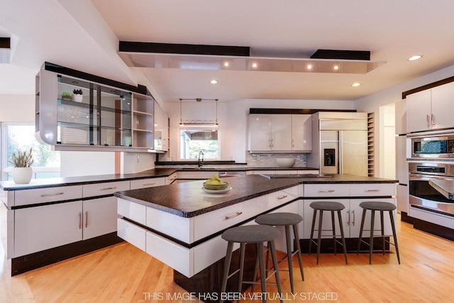 4720 Sumac Rd, Middleton, WI 53562 - kitchen with built in appliances, light wood-style flooring, dark countertops, white cabinets, and backsplash
