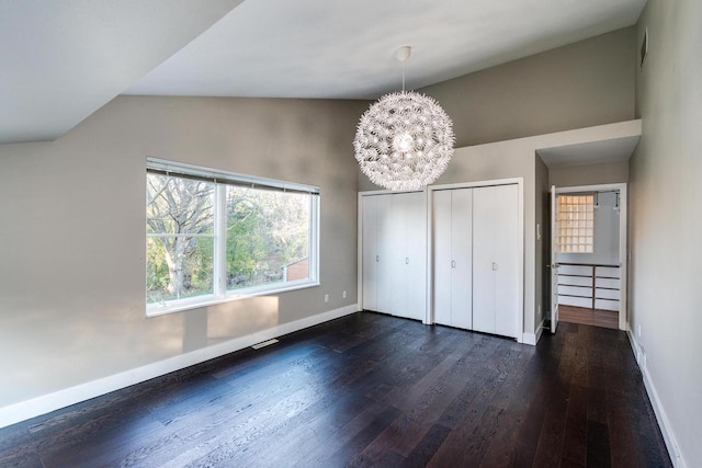 unfurnished bedroom featuring two closets, vaulted ceiling, a notable chandelier, and dark hardwood / wood-style floors