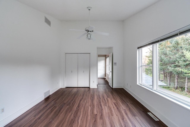 unfurnished bedroom featuring a closet, a towering ceiling, ceiling fan, and dark wood-type flooring