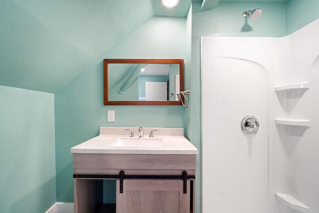 bathroom with walk in shower, vanity, and lofted ceiling