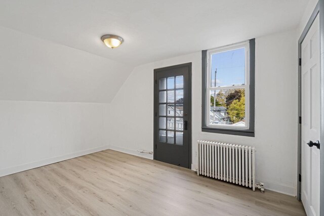 additional living space featuring radiator heating unit, light wood-type flooring, and lofted ceiling