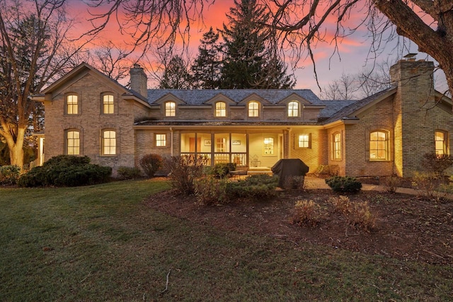 back house at dusk featuring a lawn and covered porch