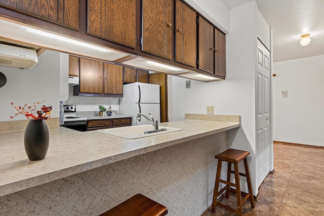 kitchen featuring stainless steel electric range, a breakfast bar, sink, white fridge, and kitchen peninsula