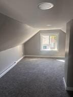 additional living space with dark colored carpet and lofted ceiling