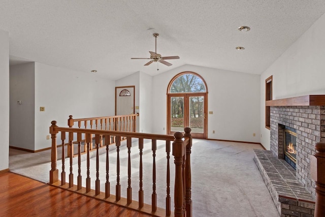 interior space featuring ceiling fan, vaulted ceiling, a brick fireplace, light hardwood / wood-style floors, and a textured ceiling