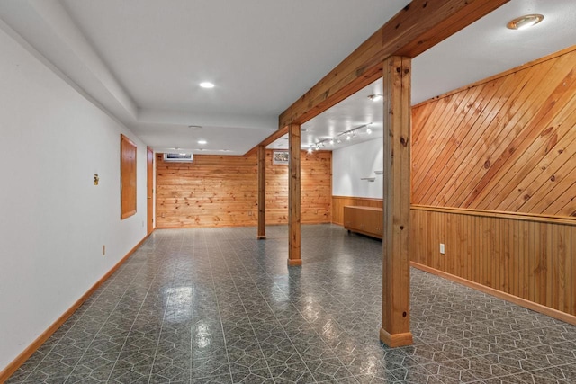 basement featuring rail lighting and wood walls