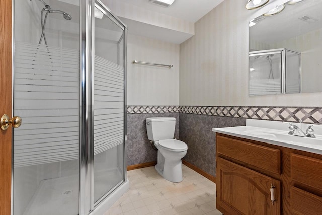 bathroom featuring toilet, vanity, tile walls, and a shower with shower door