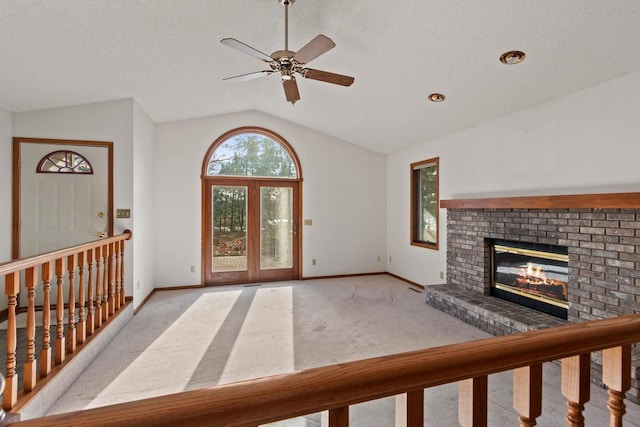 unfurnished living room with lofted ceiling, light colored carpet, ceiling fan, a brick fireplace, and a textured ceiling