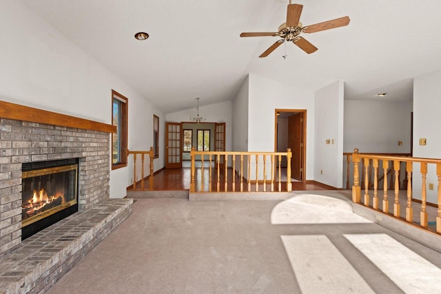 unfurnished living room featuring carpet floors, ceiling fan, vaulted ceiling, a brick fireplace, and french doors